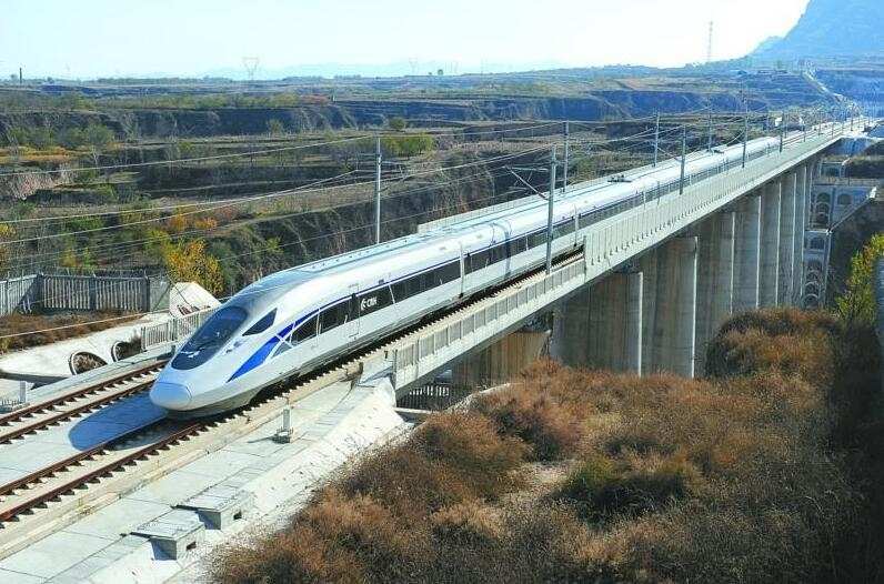 A silver and blue high-speed train travels on an elevated track over a rural, arid landscape.