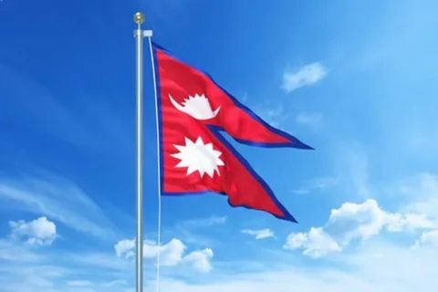 A 3D illustration of the flag of Nepal on a flagpole, waving against a bright blue sky with white clouds. The flag is the only non-quadrilateral national flag in the world, consisting of two triangular pennants joined together. It has a red field with a blue border. The upper pennant contains a stylized white moon, and the lower one has a stylized white sun.