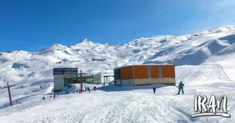 Skiers enjoying the snowy slopes at Dizin Ski Resort in the Alborz Mountains, Iran, with clear blue skies and mountain peaks in the background.