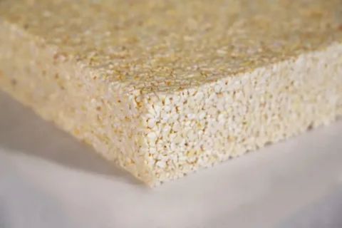 A thick, tan-colored insulation panel created from granulated and pressed popcorn kernels, showing its fine, porous texture.