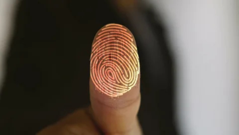 Close-up of a human finger pad touching a surface. The fingerprint is digitally illuminated with an orange-gold glowing overlay of the unique ridge pattern, suggesting a biometric scan or security feature.