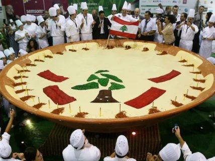 a massive, round dish of hummus being presented by a large group of chefs and officials.

The surface of the hummus is decorated with the green cedar tree and red bars of the flag of Lebanon. A small Lebanese flag is also being held near the dish.The enormous dish is a ceremonial presentation of the Guinness World Record for the largest plate of hummus.