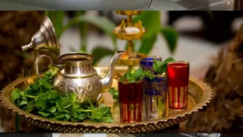 Traditional Moroccan mint tea set with a silver teapot, fresh mint leaves, and decorated glasses arranged on a brass tray.